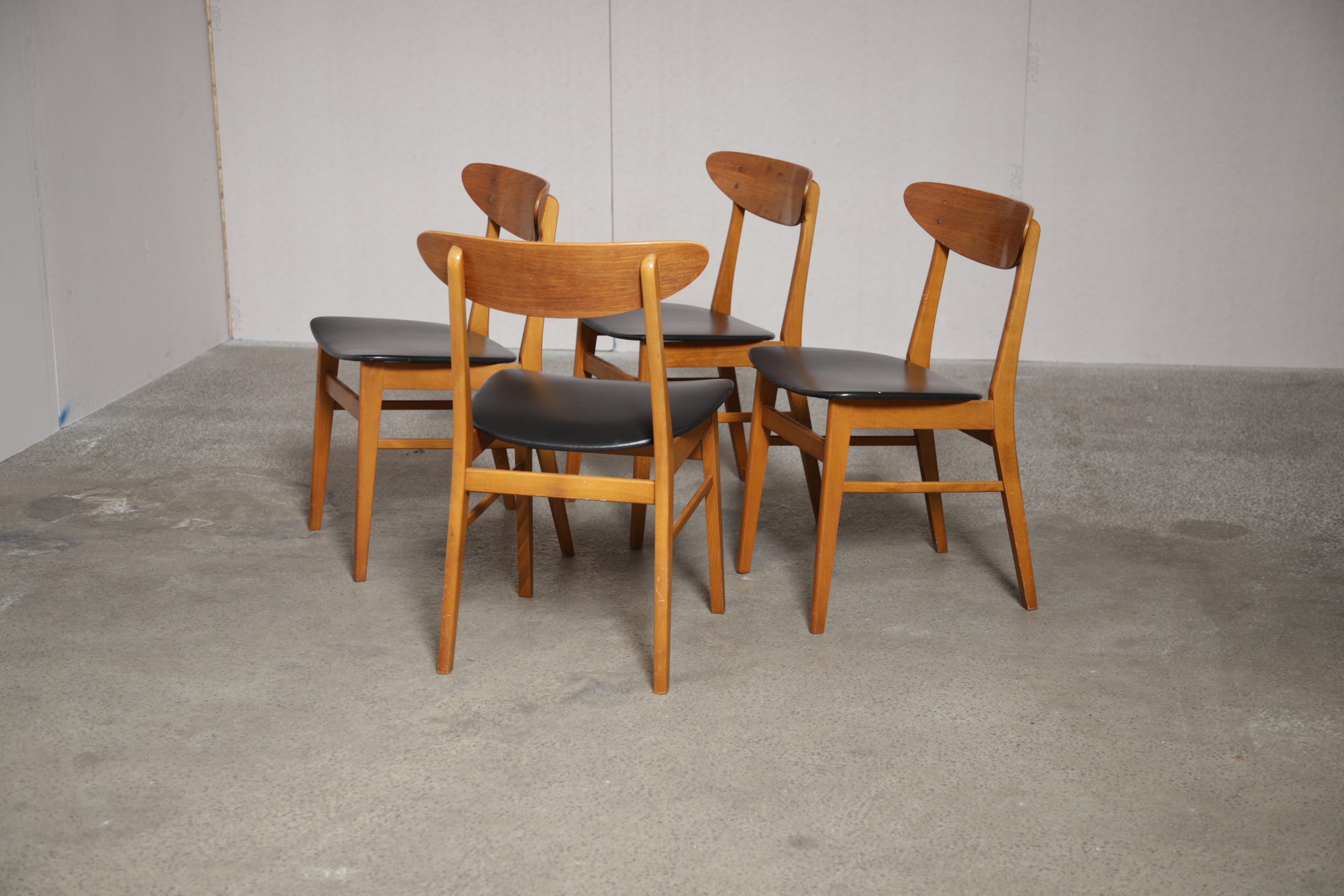 Vintage mid-century dining chairs with light wood frames and black upholstered seats.